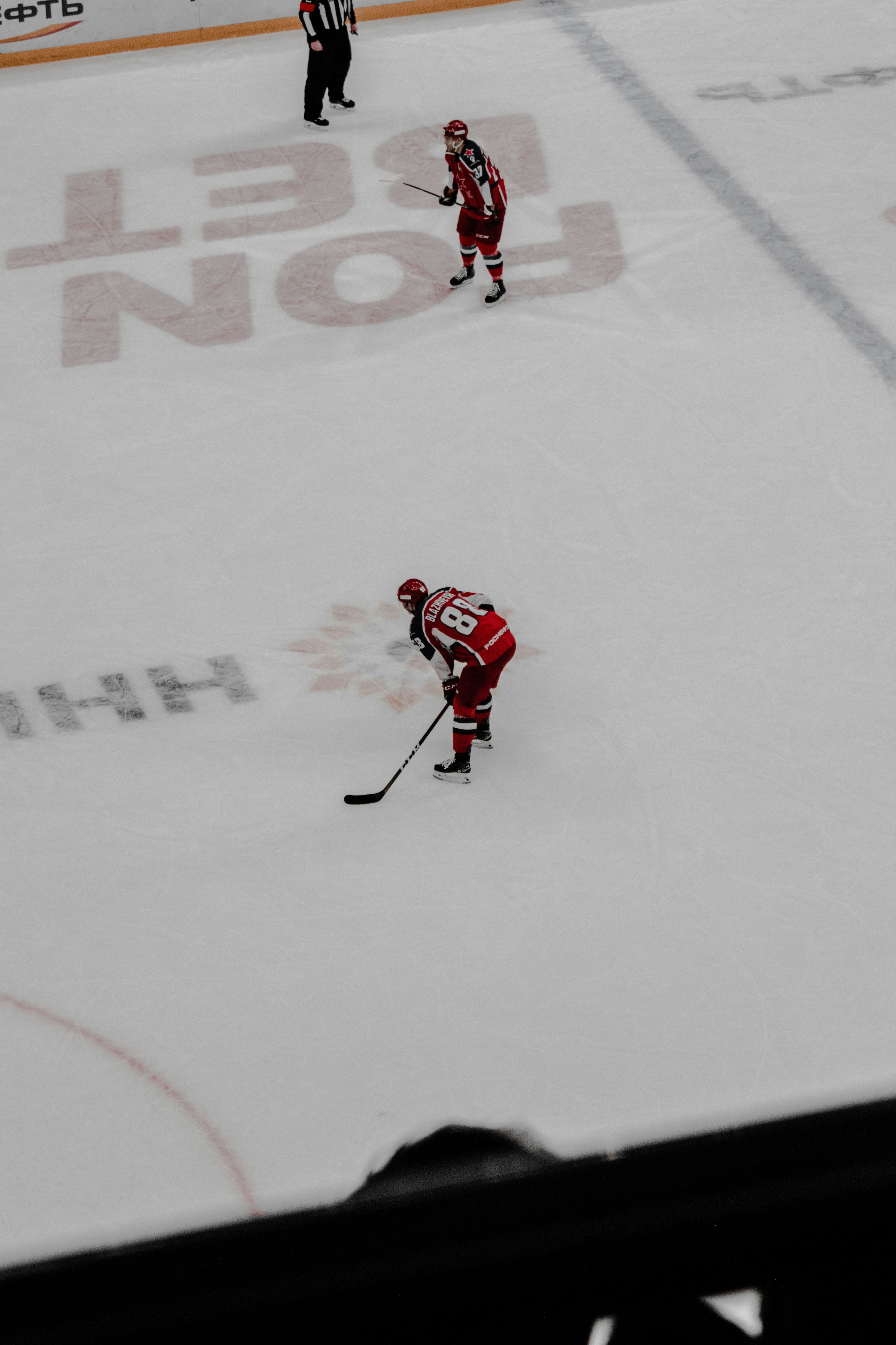man in red jersey shirt and black pants playing hockey